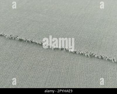 Bord déchiré de tissu de laine fine en vert ou bleu. Fils lâches au bord d'un morceau de textile. Gros plan. Fond tissé. Couleur pastel vert calme Banque D'Images