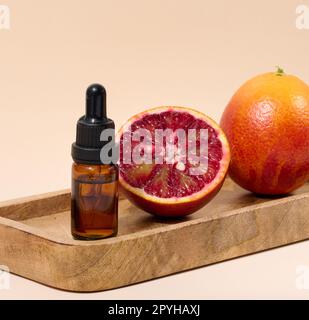 Flacon en verre brun avec pipette et moitié d'orange rouge sur fond beige, huiles et cosmétiques Banque D'Images