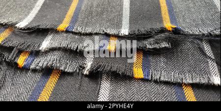 Tissu gris-noir avec rayures orange et bleues. Tissu textile plié soigneusement sur la surface. Matériau en laine naturelle pour coudre des vêtements et des tissus d'ameublement. Style de vie. Gros plan. Flou artistique Banque D'Images