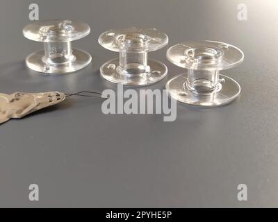 Boutonnière pour enfiler automatiquement l'aiguille de la machine à coudre. Trois bobines de machine à coudre en plastique transparent. Industrie textile. Détail de l'équipement de couture. Fond gris, rétro-éclairage Banque D'Images