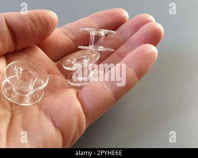 Bobines en plastique transparent d'une machine à coudre moderne dans la paume d'une femme - une couturière. Fond gris. machines à coudre Banque D'Images