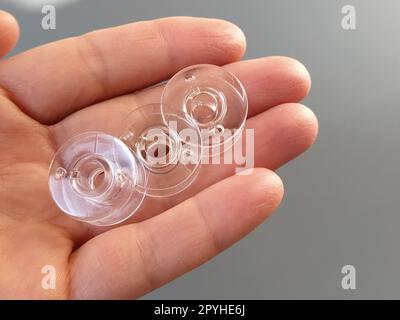 Bobines en plastique transparent d'une machine à coudre moderne dans la paume d'une femme - une couturière. Fond gris. machines à coudre Banque D'Images