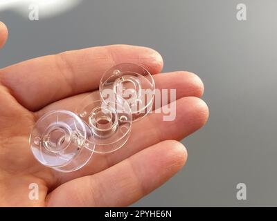 Bobines en plastique transparent d'une machine à coudre moderne dans la paume d'une femme - une couturière. Fond gris. machines à coudre Banque D'Images