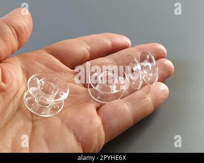 Bobines en plastique transparent d'une machine à coudre moderne dans la paume d'une femme - une couturière. Fond gris. machines à coudre Banque D'Images