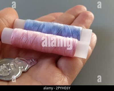 dispositif pour tirer le fil dans l'oeillet de l'aiguille. Bobines avec des fils bleus et roses en arrière-plan. Une femme tient un enfileur d'aiguille dans sa main et montre son mince œil de fil Banque D'Images
