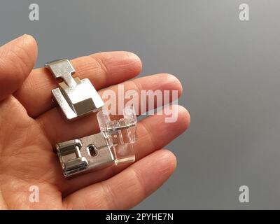 Ensemble de pieds pour une machine à coudre électrique dans une main féminine. Fond gris. Objets en métal et en plastique dans la paume de votre main. Banque D'Images