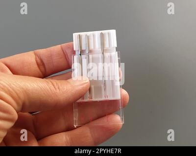 un jeu d'aiguilles de machine à coudre dans un boîtier en plastique blanc. La main d'une femme tient les aiguilles d'une machine à coudre électrique. Fond gris. Différentes épaisseurs d'aiguille Banque D'Images