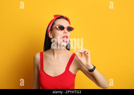 Jeune femme à la mode dans une tenue à épingler mâchant du bubblegum sur fond jaune Banque D'Images