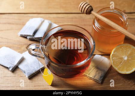 Sachet de thé dans une tasse de verre, miel et citron sur une table en bois Banque D'Images