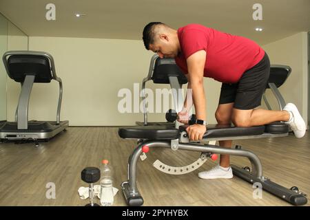 latino aux cheveux foncés exercices d'homme adulte dans une salle de gym, travail de force musculaire pour la réadaptation de physiothérapie sur le bras avec des haltères Banque D'Images