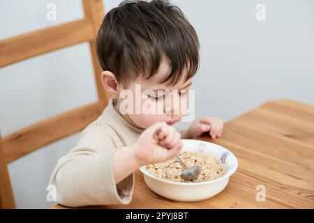 un petit garçon mange des flocons d'avoine pour le petit-déjeuner dans la cuisine Banque D'Images