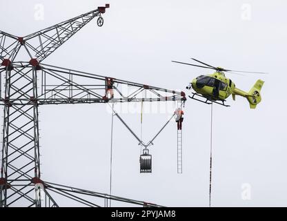 PRODUCTION - 03 mai 2023, Schleswig-Holstein, Klixbüll: Un hélicoptère vole entre les pylônes de puissance de la dernière section de construction du pipeline de la côte ouest comme les câbles de chef sont tirés dans. L'hélicoptère est utilisé pour faire voler des câbles en plastique légers d'un pôle à l'autre, tandis que les installateurs industriels guident le câble de guidage à travers les poulies aux extrémités des pôles. La ligne de la côte ouest - une ligne aérienne de 380 kilovolts - va parcourir un total d'environ 140 kilomètres entre Brunsbüttel et la frontière danoise et de là. Photo: Christian Charisius/dpa Banque D'Images