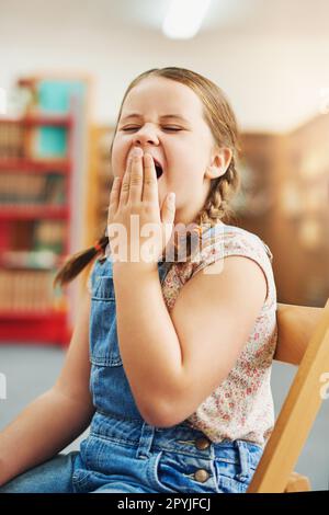 Cette classe est un peu ennuyeuse. Portrait d'une jeune fille d'école fatiguée bâillant avec sa main devant sa bouche tout en étant assise à l'intérieur d'un Banque D'Images