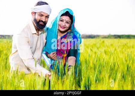 Portrait d'un couple de jeunes agriculteurs indiens heureux touchant une récolte de blé debout sur le terrain agricole par beau soleil. Copier l'espace. Le concept de l'inde rurale. Banque D'Images