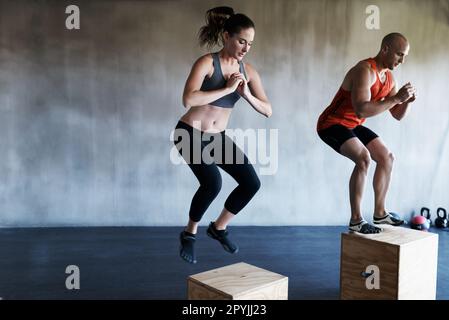 Salle de gym, fitness et personnes sur un coffret de saut pour l'entraînement, le cardio ou la routine d'entraînement sur fond de mur. Saut, exercice et femme avec entraîneur personnel pour Banque D'Images