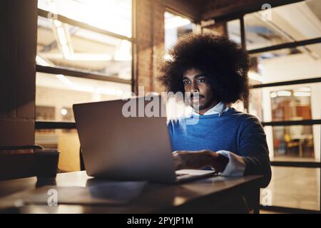 Concentré sur sa tâche immédiate. un beau jeune homme concepteur utilisant son ordinateur portable tout en travaillant tard dans le bureau. Banque D'Images