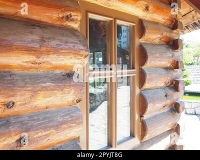 Gros plan sur une maison en rondins à la mode. Fenêtre en verre avec cadre en bois. Le mur d'un bâtiment en bois avec un auvent du toit. Banque D'Images