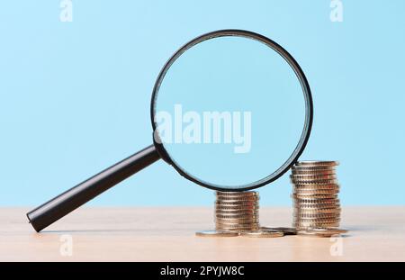 Une pile de pièces de monnaie en métal et une loupe en plastique sur fond bleu. Le concept de l'augmentation des impôts, des subventions Banque D'Images