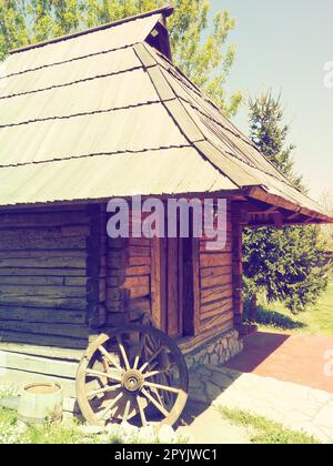 Stanisici, Bijelina, Bosnie-Herzégovine, 25 avril 2021. Ferme de village en rondins. Habitation traditionnelle de montagne bosniaque du 19e siècle. Bâtiment ethno restauré. Roue en bois antique de char Banque D'Images