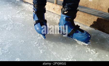 Pieds avec patins. Uniformes et équipement de sport. Patinoire. De longues ombres sur la glace du bas soleil d'hiver. Banque D'Images