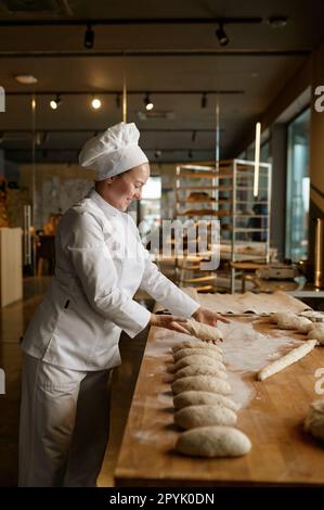 Femme boulangère formant des pains à partir de pâte crue dans une cuisine professionnelle Banque D'Images