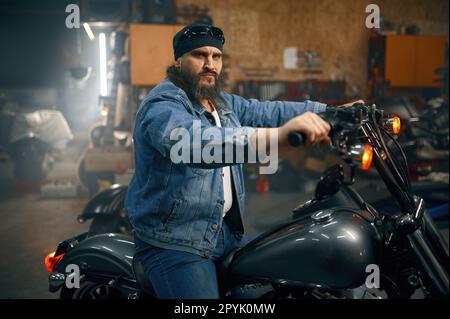 Portrait d'un motard à la barbe mûre sur la moto au-dessus de l'intérieur du garage Banque D'Images