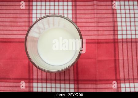 Un verre de lait se dresse sur un chiffon rouge à carreaux, vue du dessus Banque D'Images