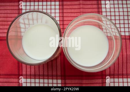 Deux verres de lait se tiennent sur un chiffon rouge à carreaux, vue du dessus Banque D'Images
