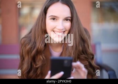 Femme heureuse sur un banc te regarde tenant le téléphone Banque D'Images