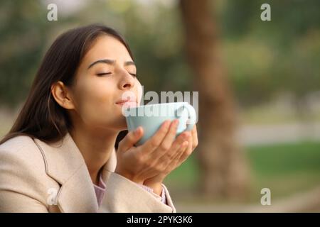 Femme en hiver sentant l'arôme de café dans un parc Banque D'Images