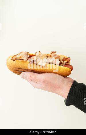 Vue recadrée de jeune gars tenant le hot-dog savoureux avec de la moutarde et du ketchup sur fond blanc. Street food, livraison. Banque D'Images