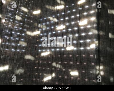 La lumière du soleil brille à travers des stores avec de petits trous et des rideaux gris - tulle. Image abstraite. L'été. Réflexion des taches de lumière sur le tissu Banque D'Images