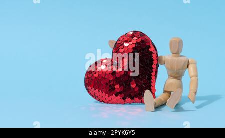 Mannequin en bois et cœur rouge en paillettes sur fond bleu Banque D'Images
