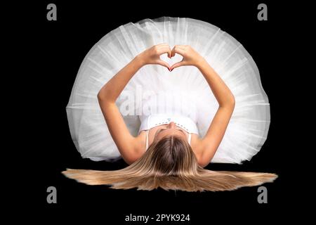 ballerine dans une robe blanche se trouve sur le sol et montre un coeur avec ses mains, portrait sur un fond noir Banque D'Images
