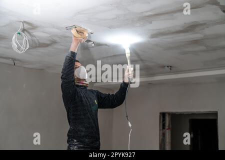 ponçage d'un plafond en placoplâtre dans un nouveau bâtiment avec une truelle Banque D'Images