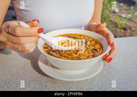Une fille mange de la soupe chinoise aigre et chaude ou de la soupe épicée de Taïwan avec des ingrédients frais sur une assiette au restaurant. Cuisine et plats asiatiques traditionnels Banque D'Images