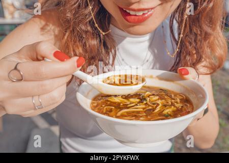 Une fille mange de la soupe chinoise aigre et chaude ou de la soupe épicée de Taïwan avec des ingrédients frais sur une assiette au restaurant. Cuisine et plats asiatiques traditionnels Banque D'Images