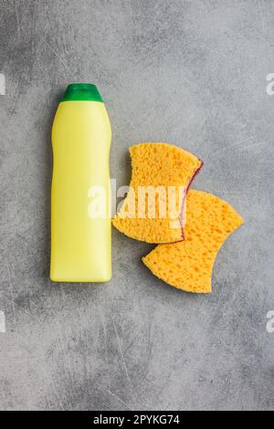 Éponge pour laver la vaisselle, bouteille en plastique et assiettes sur la table grise de la cuisine. Vue de dessus. Banque D'Images