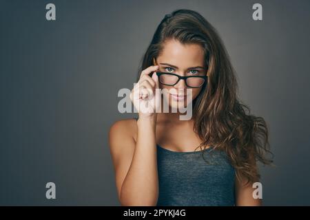 Ce qui importe le plus, c'est la façon dont vous vous voyez. Photo en studio d'une jeune femme attirante qui se pend sur ses lunettes sur un fond gris. Banque D'Images