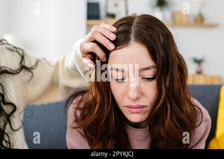 Jeune femme adulte soutenant une triste amie assise sur un canapé à la maison Banque D'Images