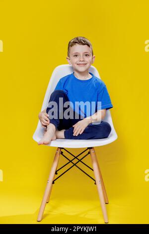 Joyeux petit garçon assis sur un fauteuil jaune - Portrait vif et ludique. Banque D'Images