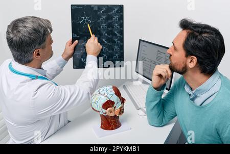 Homme avec migraine et mal de tête en consultation avec le neurologue qui regarde l'ARM de la tête du patient pour analyser sa santé du cerveau. IRM cérébrovasculaire Banque D'Images