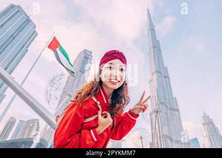 Une jeune fille asiatique heureuse qui se pose contre le drapeau des Émirats arabes et le légendaire gratte-ciel Burj Khalifa Banque D'Images