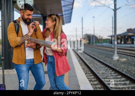 Le couple heureux est debout à la gare et attend l'arrivée de leur train. Ils regardent la carte. Banque D'Images