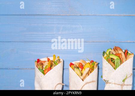 Classique rue nourriture shawarma ou burrito, sandwich sain enveloppé dans la tortilla pain plat avec viande de poulet frite, légumes frais, sauce, sur b vif Banque D'Images