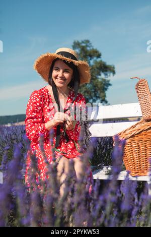 une jeune femme dans un chapeau de paille est assise sur un banc blanc dans un champ de lavande et porte une couronne Banque D'Images