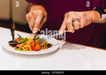 La femme mange des pâtes italiennes avec de la tomate à l'aide d'un couteau et d'une fourchette. Banque D'Images