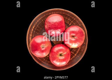 Quatre pommes rouges dans une assiette en argile sur fond noir, vue de dessus. Banque D'Images