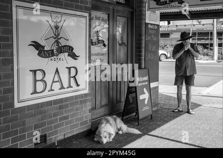 Un chien endormi et un homme éclairant une cigarette dans un coin de rue à Mareeba, Queensland, Australie Banque D'Images