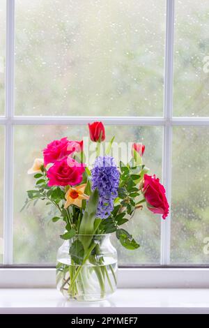 Un vase de fleurs printanières (jacinthe, roses, jonquilles et tulipes) sur un rebord de fenêtre. Banque D'Images